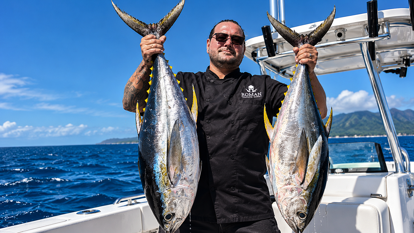 Chef Roman holding two fresh fish aboard a boat in Cayman